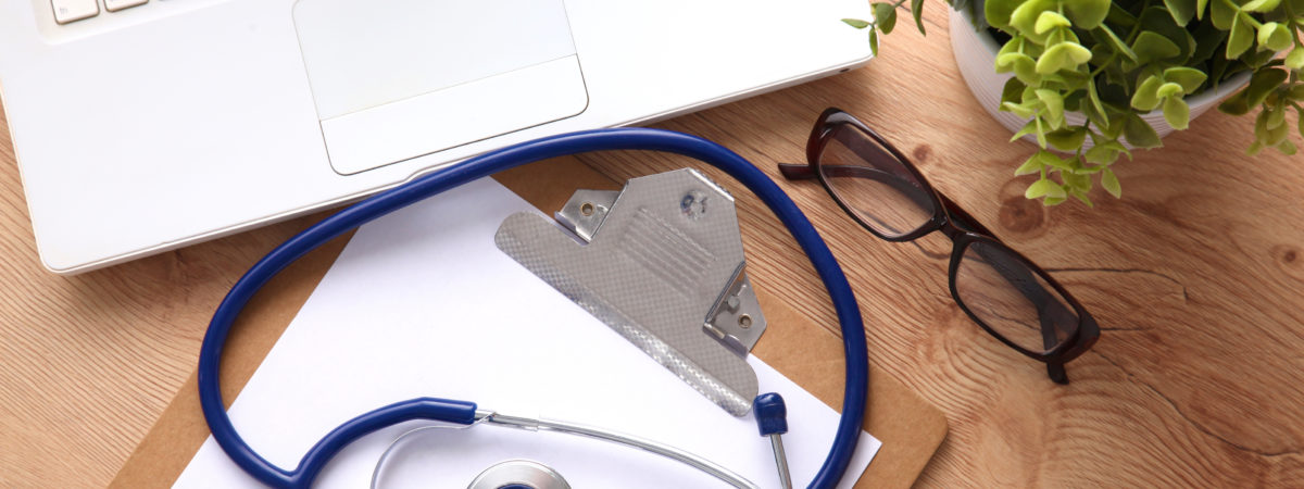 A medical stethoscope near a laptop on a wooden table, on white