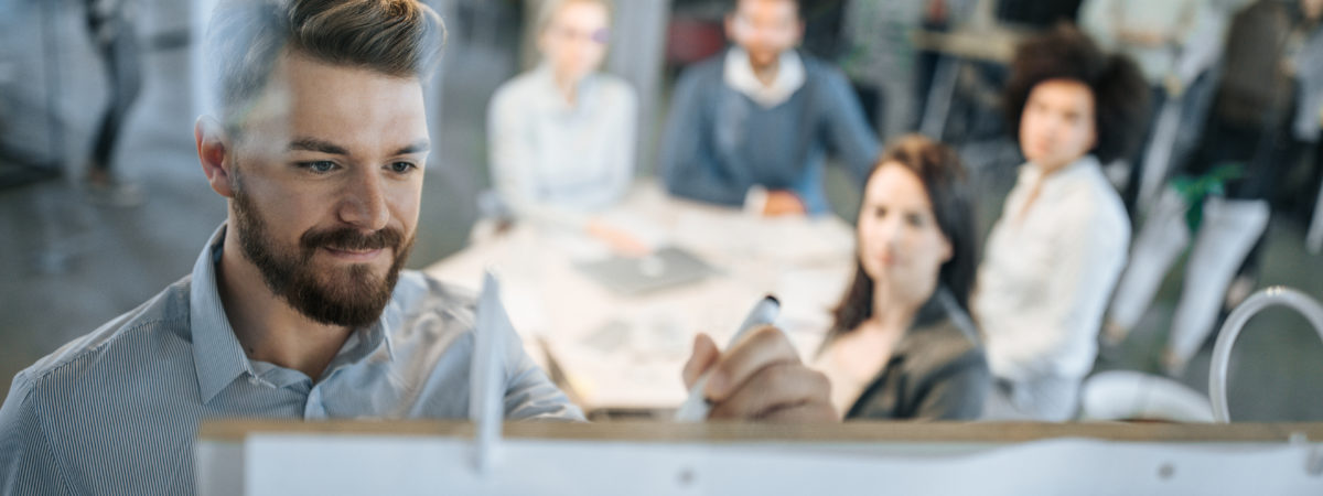 Young businessman writing ideas on whiteboard during a meeting with his colleagues.