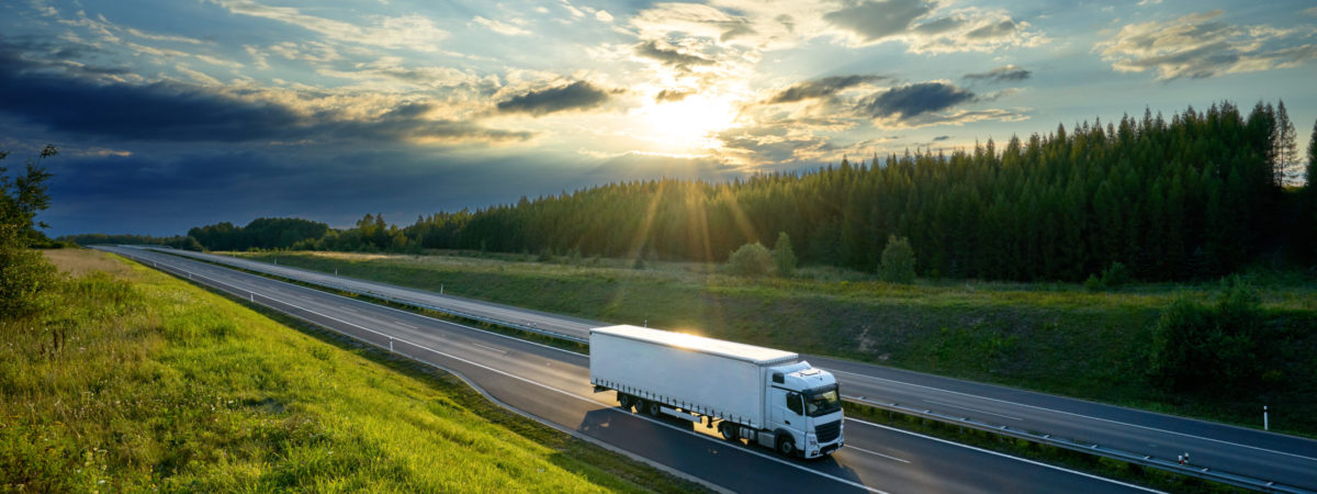 White truck driving on the highway in the countryside in the rays of the sunset with dramatic clouds