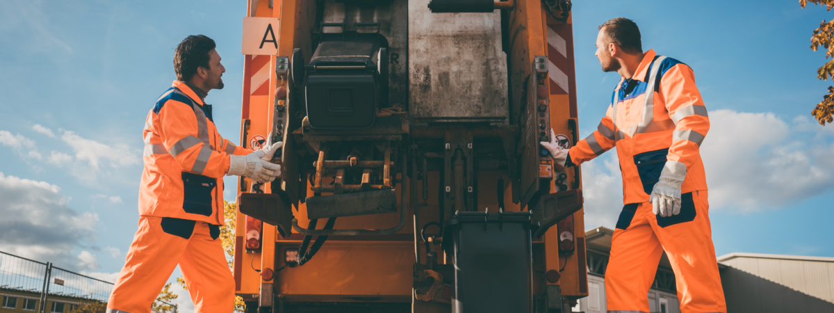 Two refuse collection workers loading garbage into waste truck